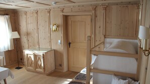 Una habitación de madera con literas, una mesita pequeña y un armario.