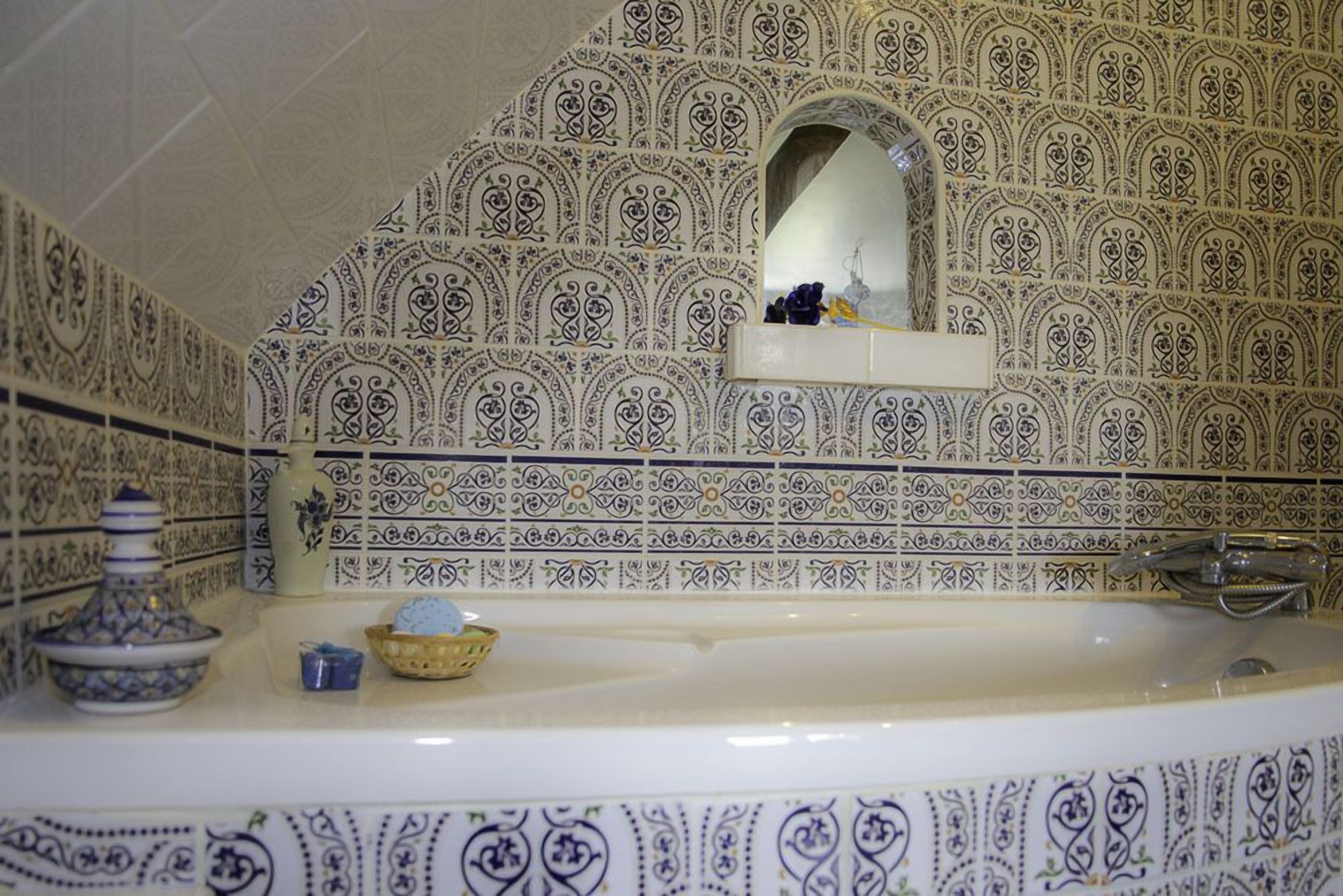 A bathroom with ornate tile patterns, a bathtub, a sink, and a mirror.