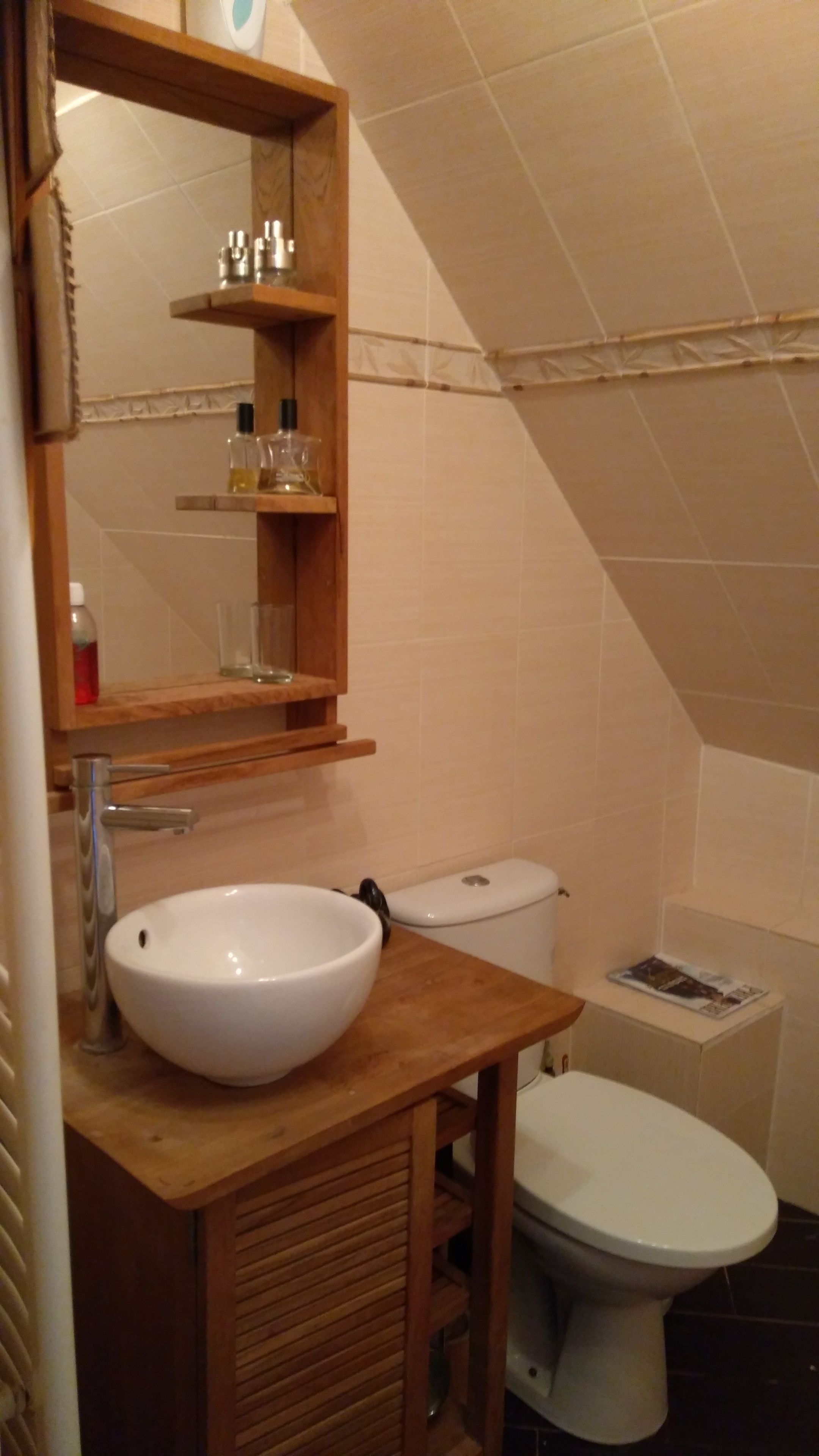Een badkamer met een houten wastafelmeubel, een witte wasbak, een toilet en een spiegel boven het meubel.