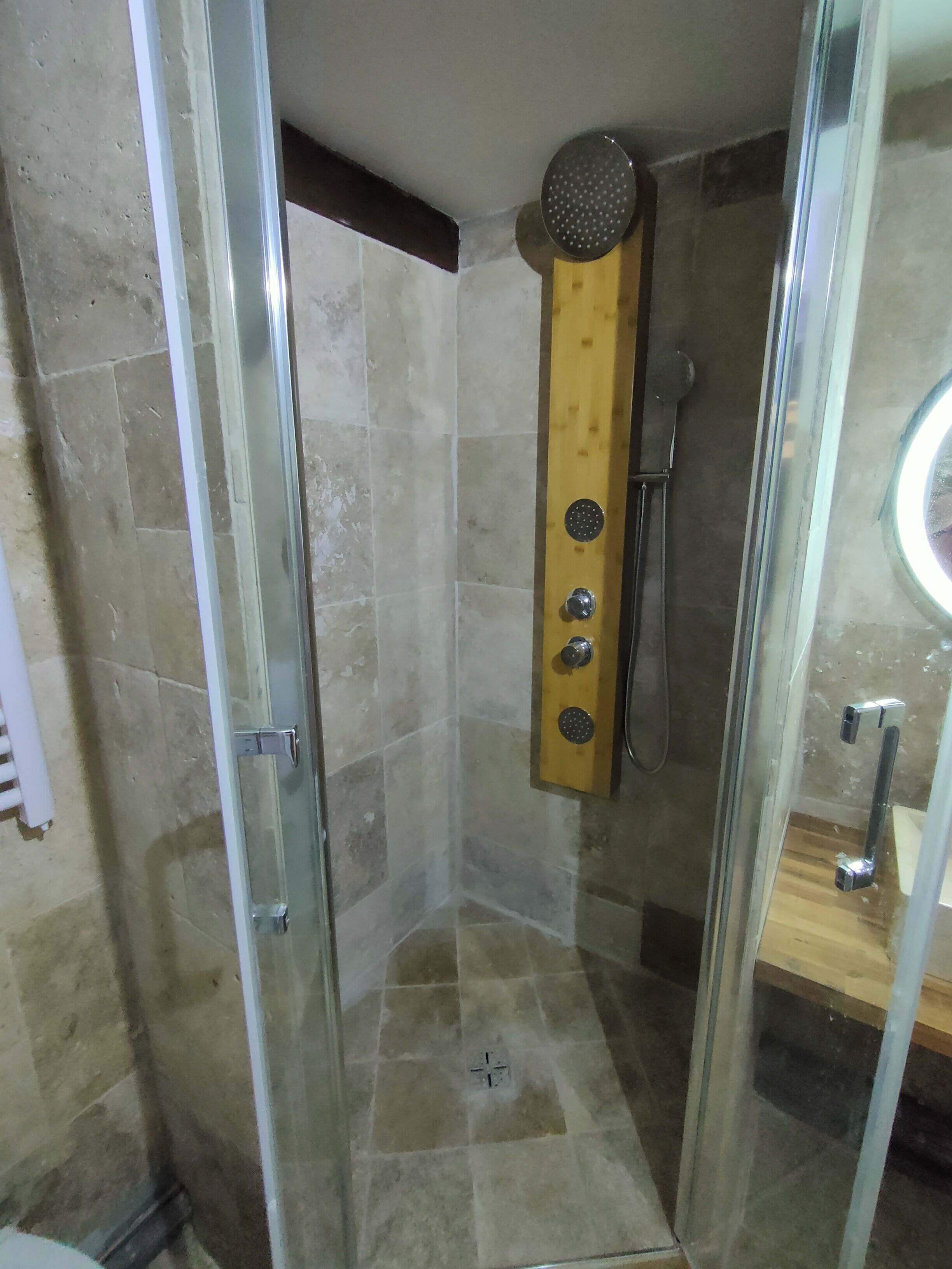 A glass-enclosed shower stall with a wooden panel, a handheld showerhead, and a handheld shower attachment.