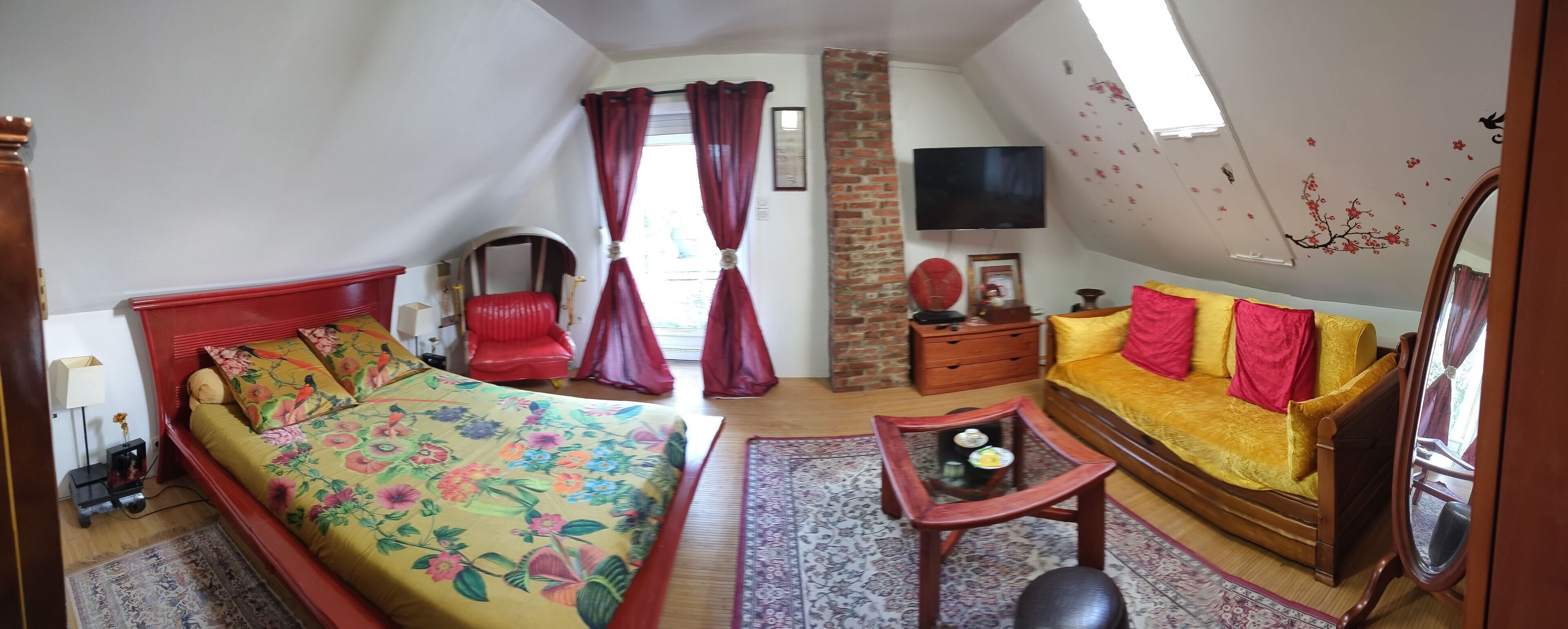 Un dormitorio con cama, sofá, sillón, televisión y espejo.