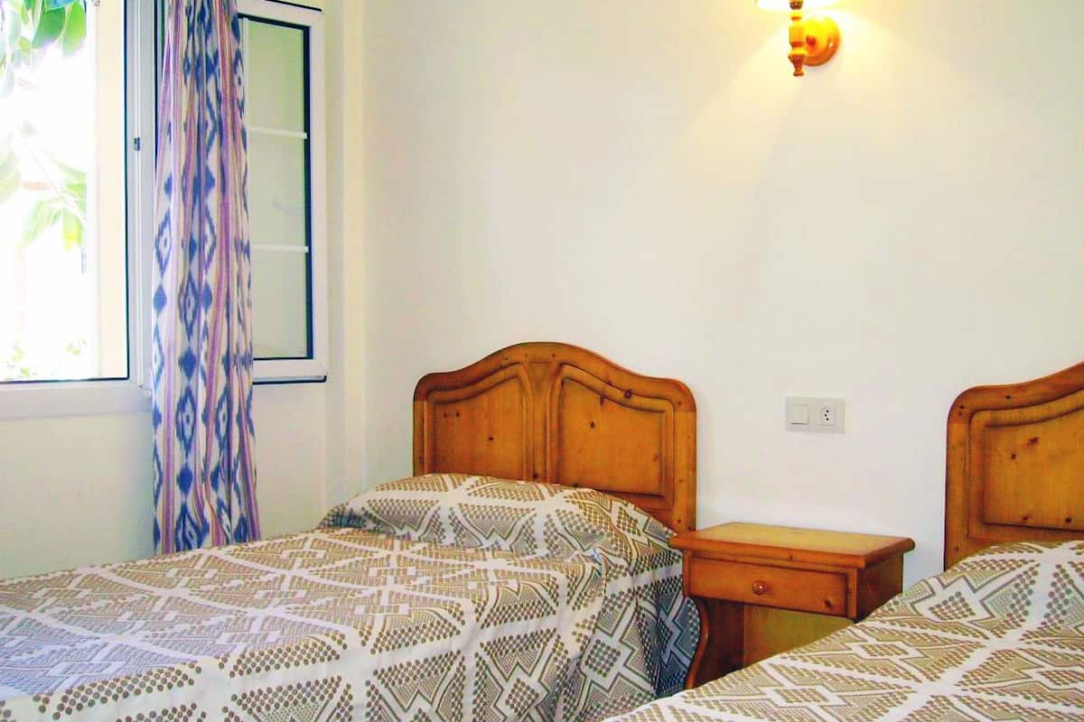 Une chambre avec deux lits en bois, une table de chevet et une lampe fixée au mur.