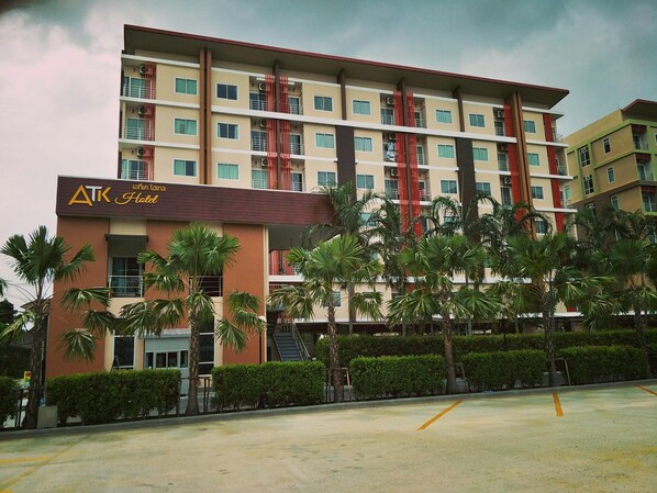 Un hotel de varios pisos con balcones, palmeras y un estacionamiento.