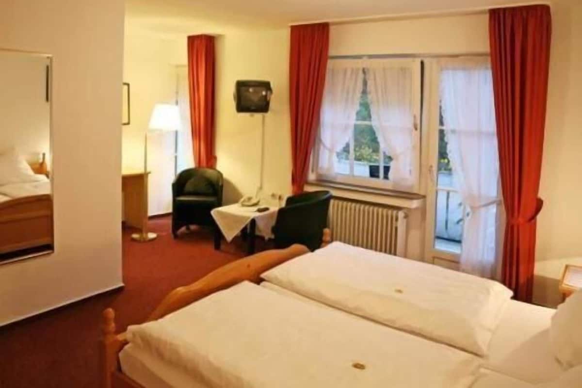 A hotel room with a bed, a chair, a table, a lamp, and a window with curtains.