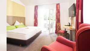 A hotel room with a bed, a TV, a chair, and a table with a kettle and glasses.