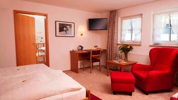 A hotel room with a bed, a desk, a chair, a TV, and a window with curtains.