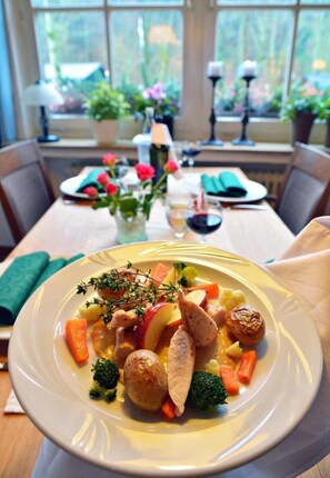 A dining table with a plate of food, a vase with flowers, and a window view. - Hotel Restaurant Haus Dumicketal (Drolshagen)