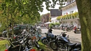A row of motorcycles parked in a driveway, with a building in the background.