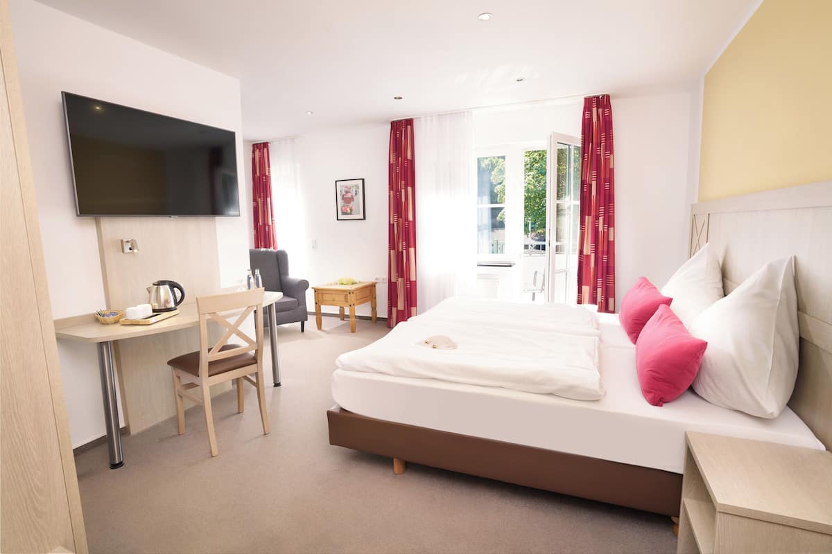 A hotel room with a bed, a desk, a chair, a TV, and a window with curtains.