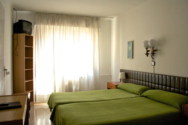 A hotel room with two beds, a television on a shelf, a lamp, and a painting on the wall.