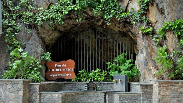 A stone entrance with a sign reading "Font del Roc del Metge" and a temperature of 70°C. - Hotel Siracusa (Escaldes-Engordany)