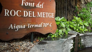A wooden sign with the text "Font del ROC DEL METGE" and "Aigua Termal 70°C". - Hotel Siracusa (Escaldes-Engordany)