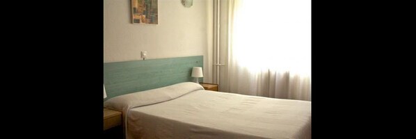 Een hotelkamer met een bed, nachtkastje, lamp en een schilderij aan de muur.