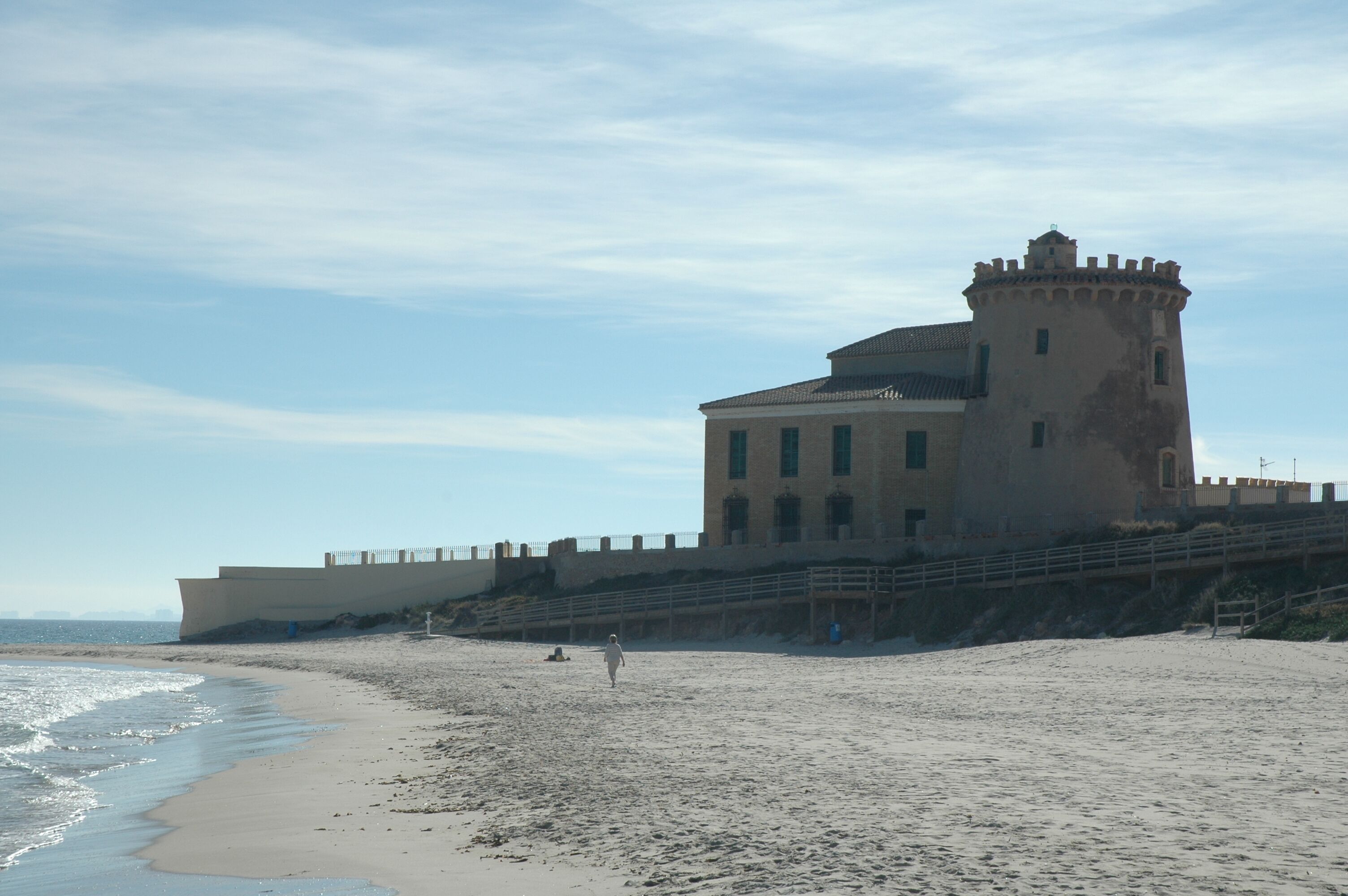 A coastal building with a tower, adjacent to a sandy beach.