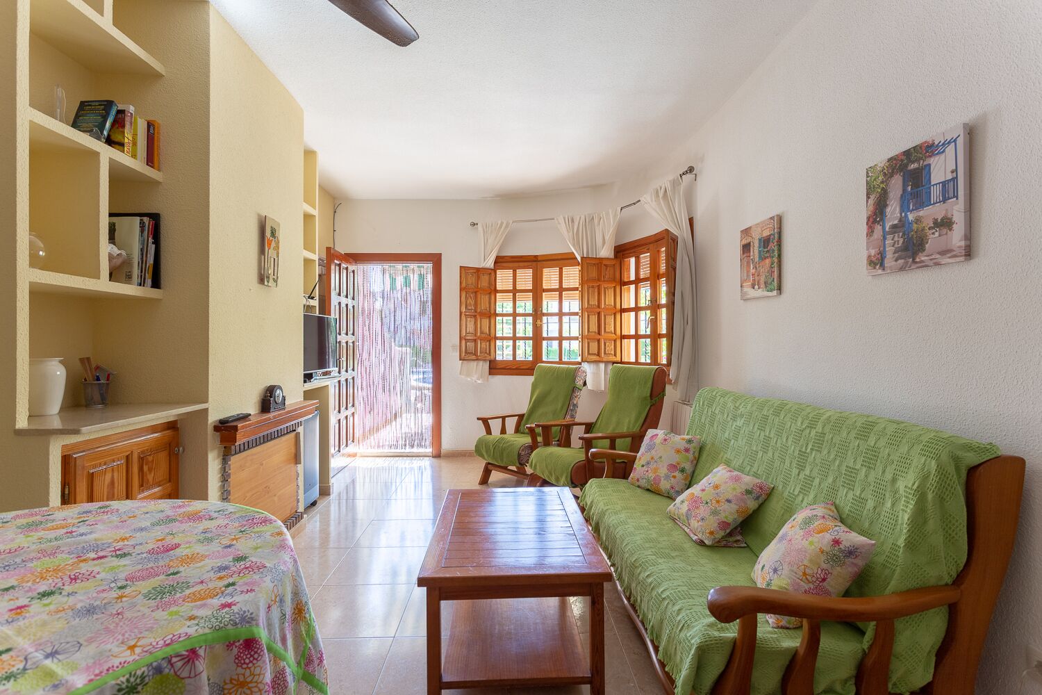 Una sala de estar acogedora con un sofá verde, sillas de madera, una mesa de madera y un televisor sobre una estantería.