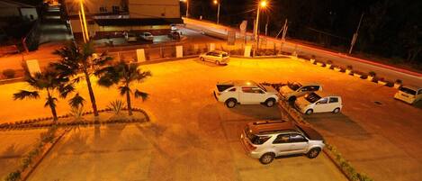 Un estacionamiento con varios coches, palmeras y un edificio al fondo.