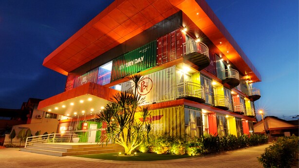 Un edificio de varios pisos con un diseño arquitectónico singular que utiliza contenedores marítimos de gran tamaño como estructura principal.