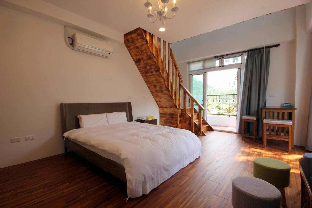 Ein Schlafzimmer mit einem großen Bett, Holzboden, einer Treppe, einem Balkon und einem kleinen Tisch.