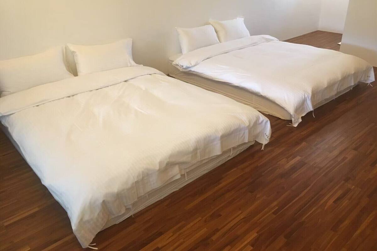 Ein Zimmer mit zwei Betten, Holzboden und weißen Wänden.