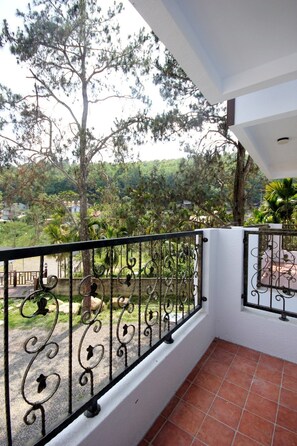 A balcony with a wrought iron railing, a tiled floor, and a view of a green landscape with trees and buildings in the distance. - Song Yue Bed & Breakfast (Yuchi)