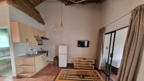 A compact living space with a kitchenette, a flat-screen TV, a sofa, and a sliding glass door to a balcony. - Qabuleka bnb (Nongoma)
