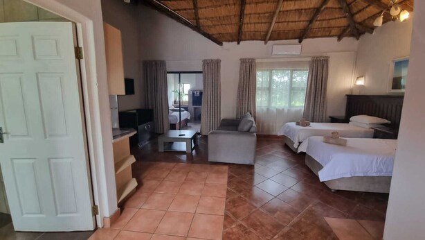 A hotel room with a thatched roof, a sofa, a bed, and a TV. - Qabuleka bnb (Nongoma)