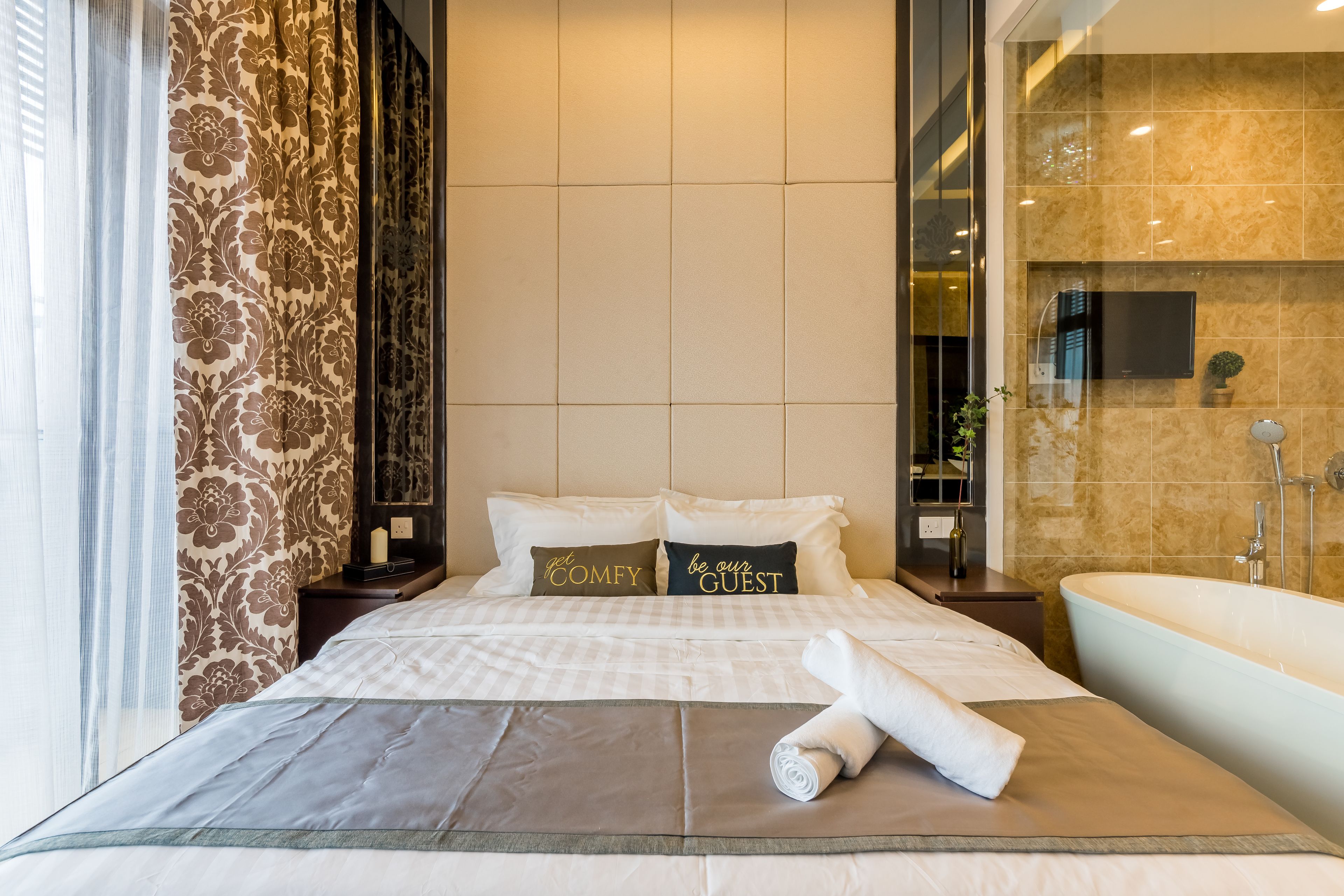 Habitación de hotel con una cama grande, un baño con bañera y un televisor en la pared.