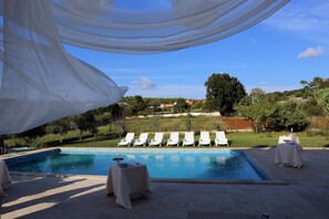 A pool area with lounge chairs and tables, surrounded by greenery and a clear sky. - Apartments Seherzada (Medulin)