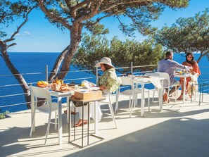 Une terrasse avec des tables et des chaises blanches, donnant sur la mer, et une table dressée pour un repas.
