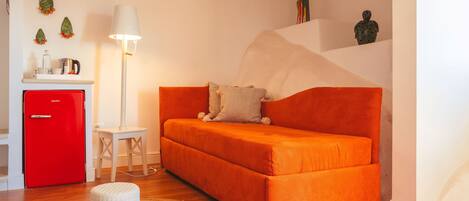 Una sala de estar moderna con un mini refrigerador rojo, una lámpara blanca y un sofá naranja brillante.