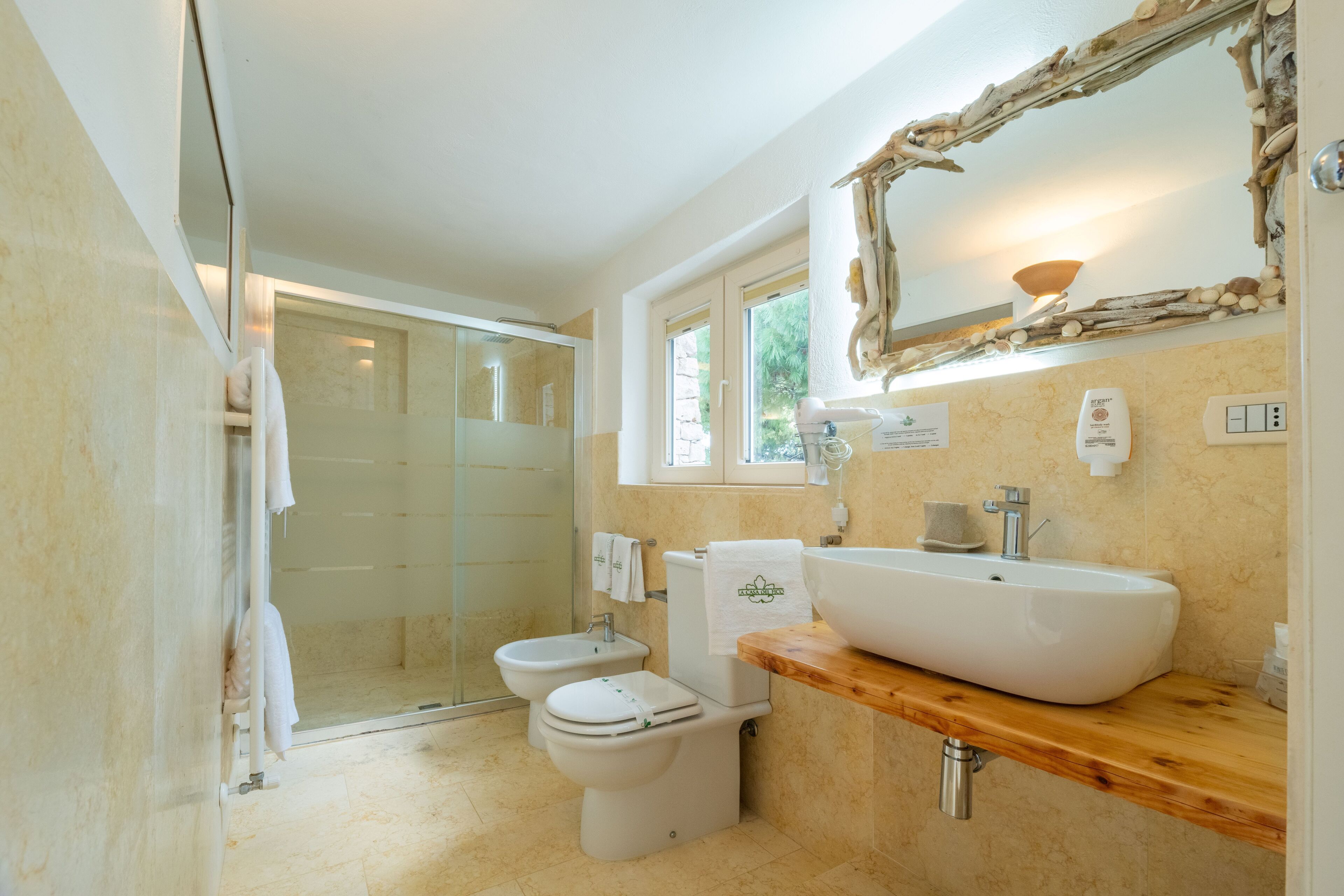 A modern bathroom with a glass shower enclosure, a white toilet, a bidet, and a wooden vanity with a large sink.
