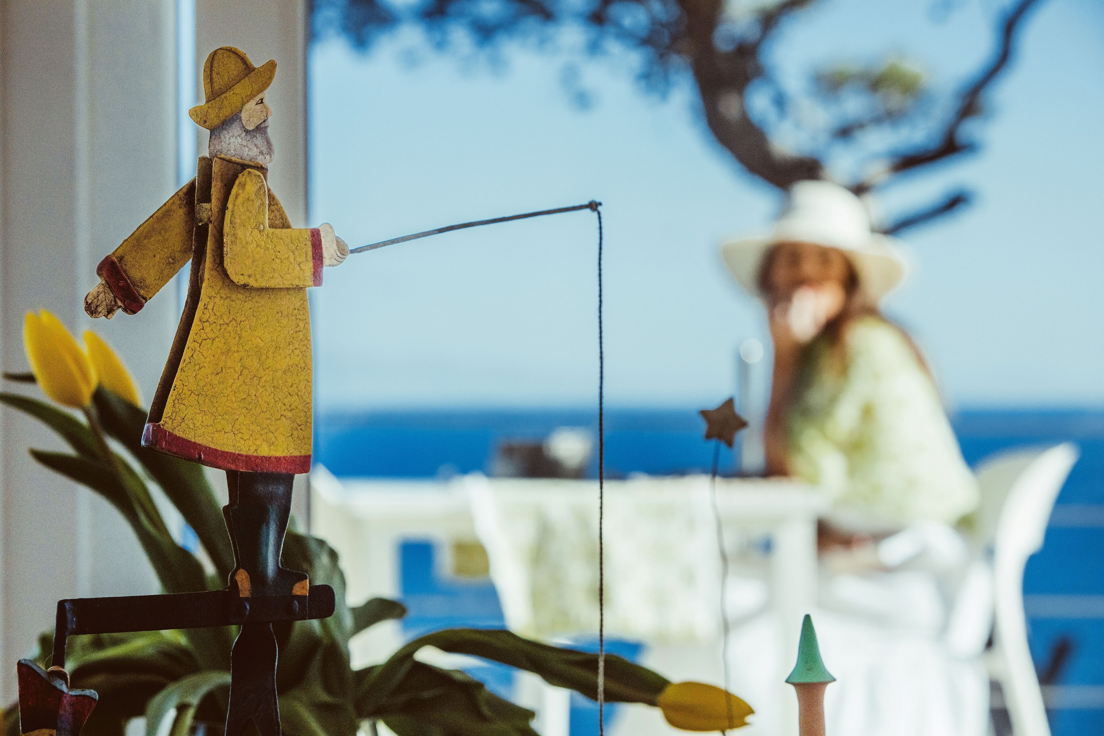 A figurine of a person fishing, a dining table, and a person in the background.