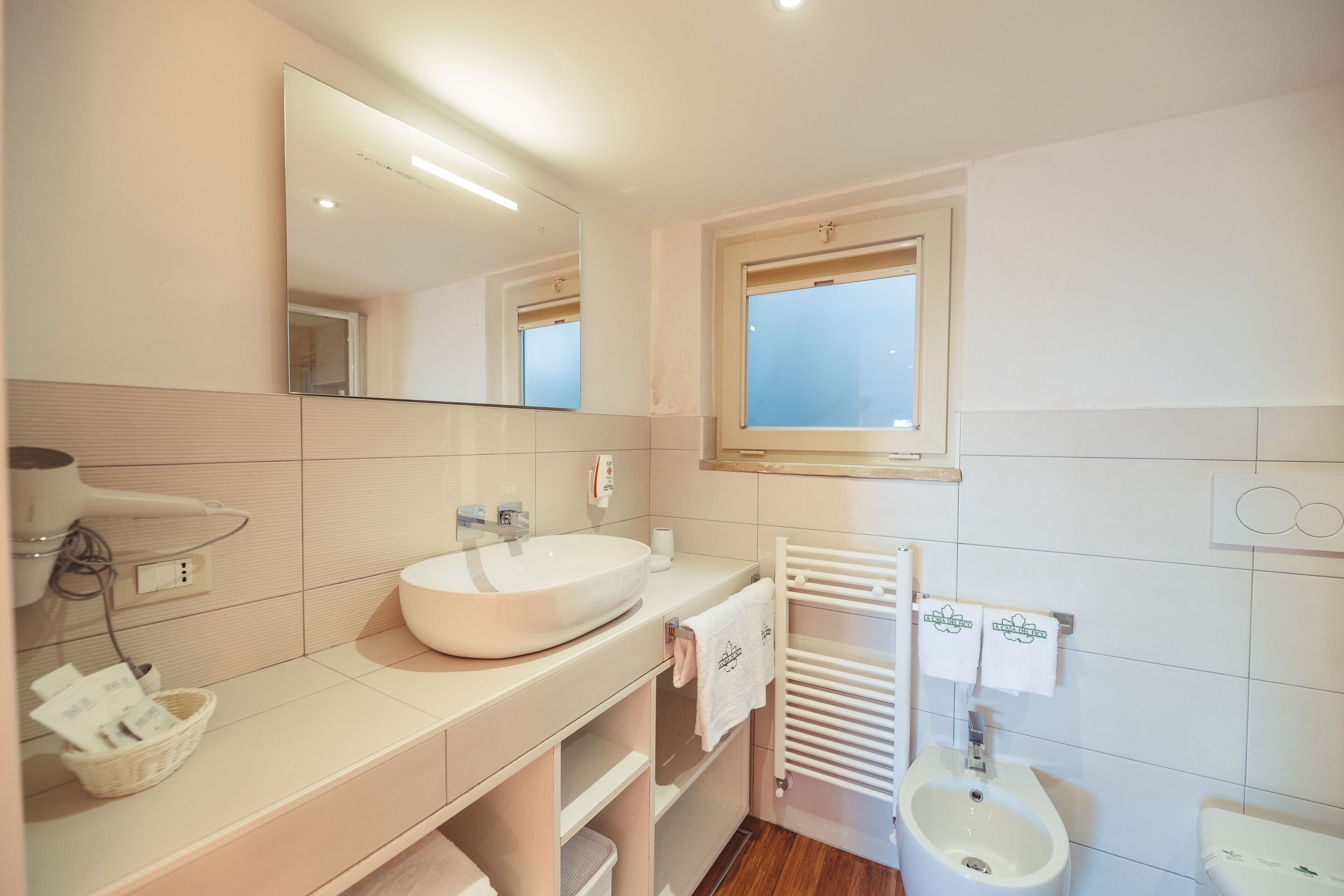 A modern bathroom with a large mirror, a sink, a bidet, and a towel rack.