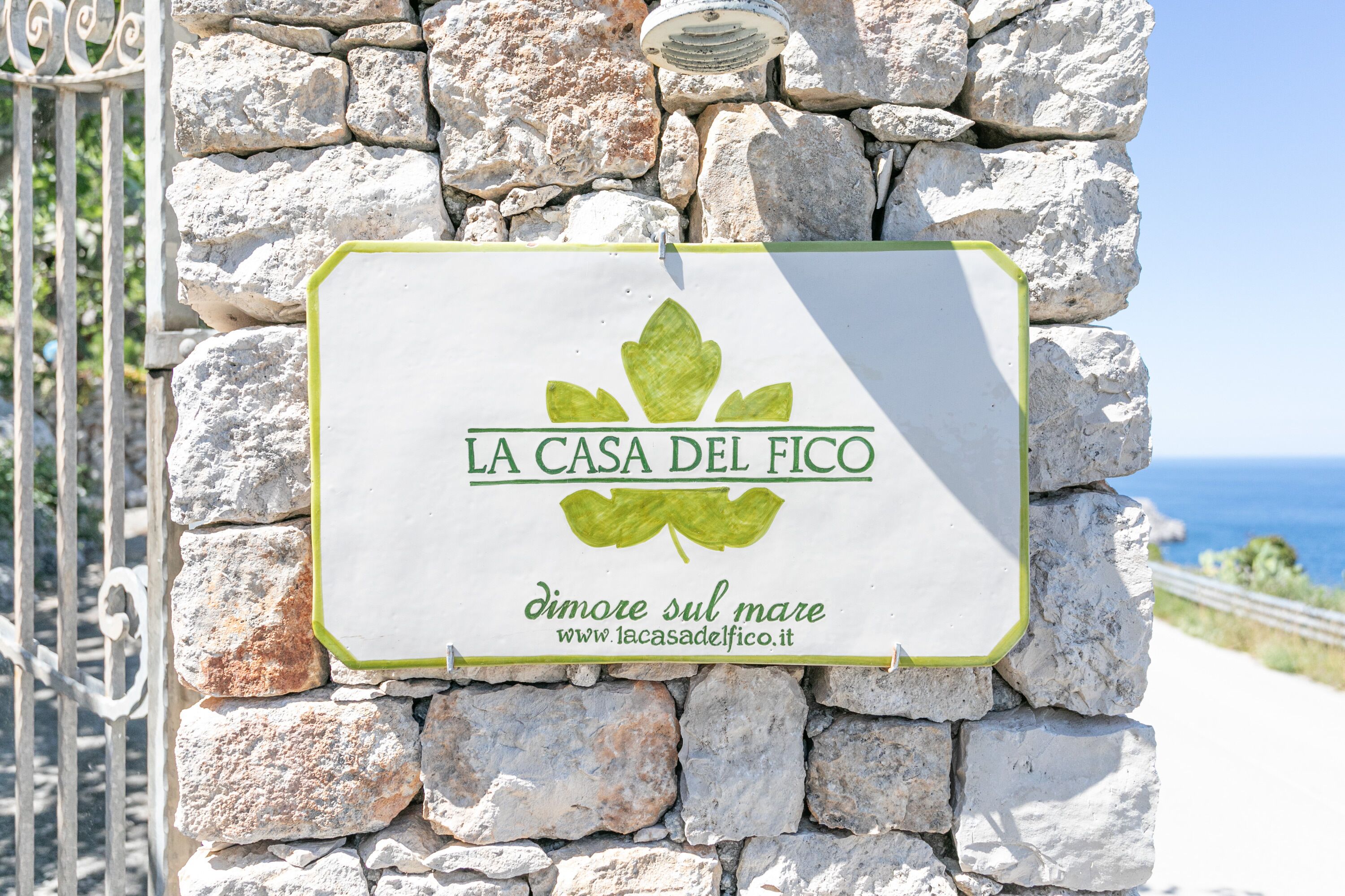 A stone wall with a sign that reads "LA CASA DEL FICO" and "dimore sul mare" with a website address.