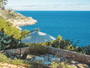 Une terrasse avec un mur en pierre, une table et une chaise, offrant une vue sur la côte.