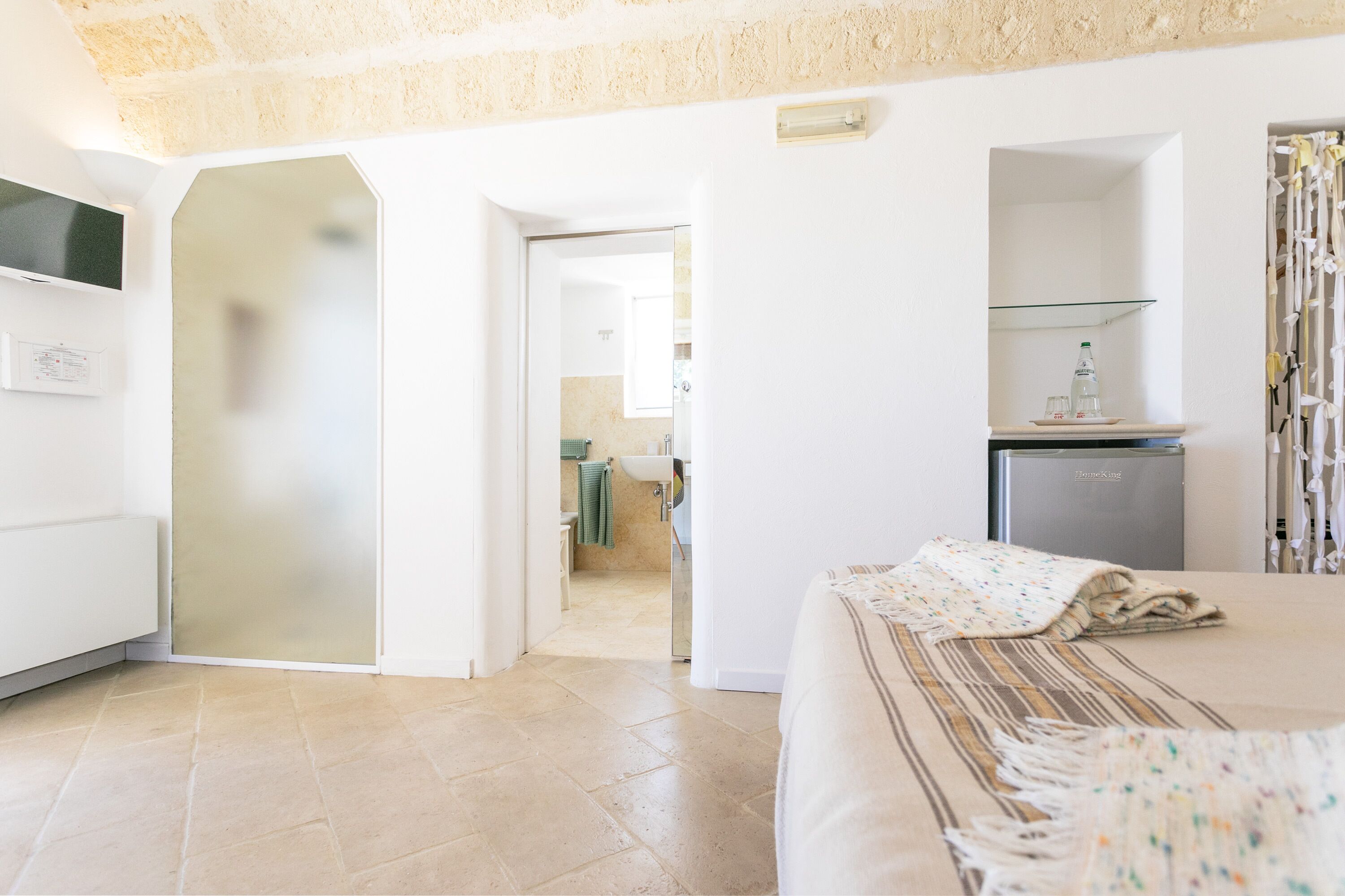 A hotel room with a bed, a TV, a refrigerator, and a bathroom visible through an open door.