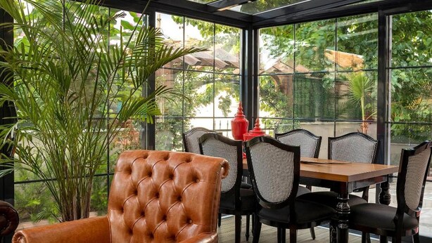 A conservatory with a leather armchair, dining table, and chairs, surrounded by large windows and potted plants. - LP Lagun Palas (Altinova)