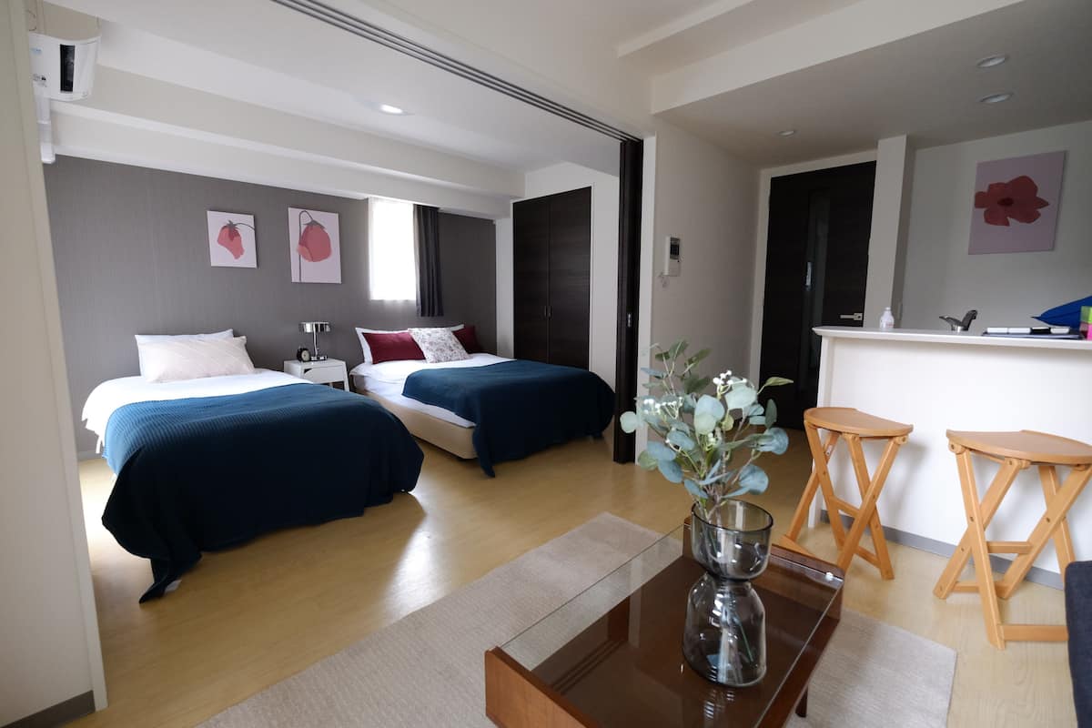 Habitación de hotel con dos camas, un escritorio, una silla, una mesita con un florero y un espejo.
