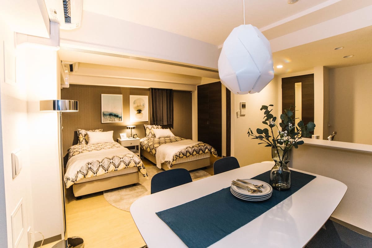 Habitación de hotel con dos camas, una mesa de comedor y un florero, y un espejo en la pared.