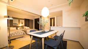 Quarto de hotel moderno com área de refeições, cama com roupa de cama estampada, mesa de cabeceira com abajur e um vaso com flores.