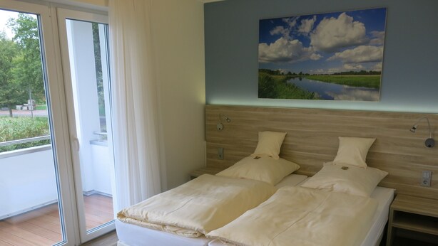 A double bed with a wooden headboard, a nightstand, and a painting of a landscape on the wall. - Landgasthaus Stärk-Berding (Steinfeld)