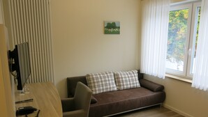A cozy living room with a brown sofa, a small table with a telephone, and a window with curtains. - Landgasthaus Stärk-Berding (Steinfeld)