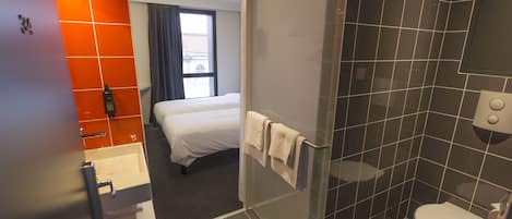 Un baño de hotel con ducha, inodoro y una cama en la habitación contigua.