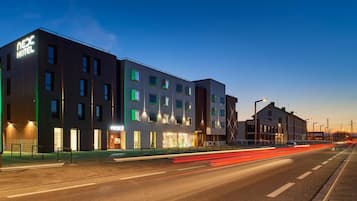 Een modern hotel met meerdere verdiepingen, grote ramen en een opvallend 'NEXC HOTEL' bord.
