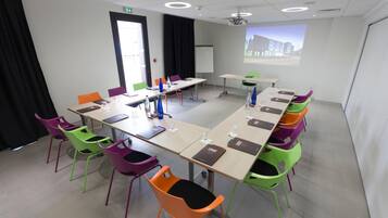 A conference room with a large table, colorful chairs, a projector screen, and a whiteboard.