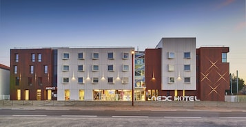 A modern hotel with multiple floors, a prominent entrance, and a visible sign for 'NEXC HOTEL'.