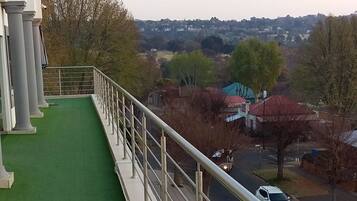 A green artificial turf walkway with metal railings, overlooking a road with cars and buildings in the distance.