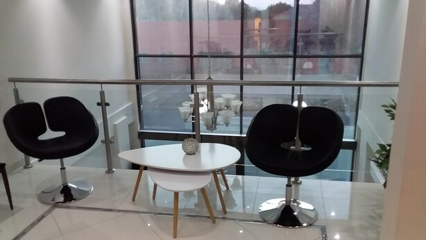 Ein modernes Interieur mit Glastrennwand, zwei schwarzen Stühlen, einem weißen Tisch und einer Tischdekoration.