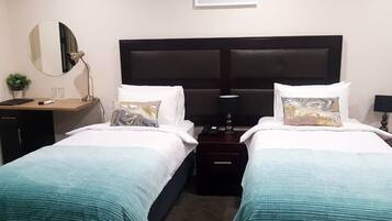 A hotel room with two beds, a desk, a mirror, and a nightstand.