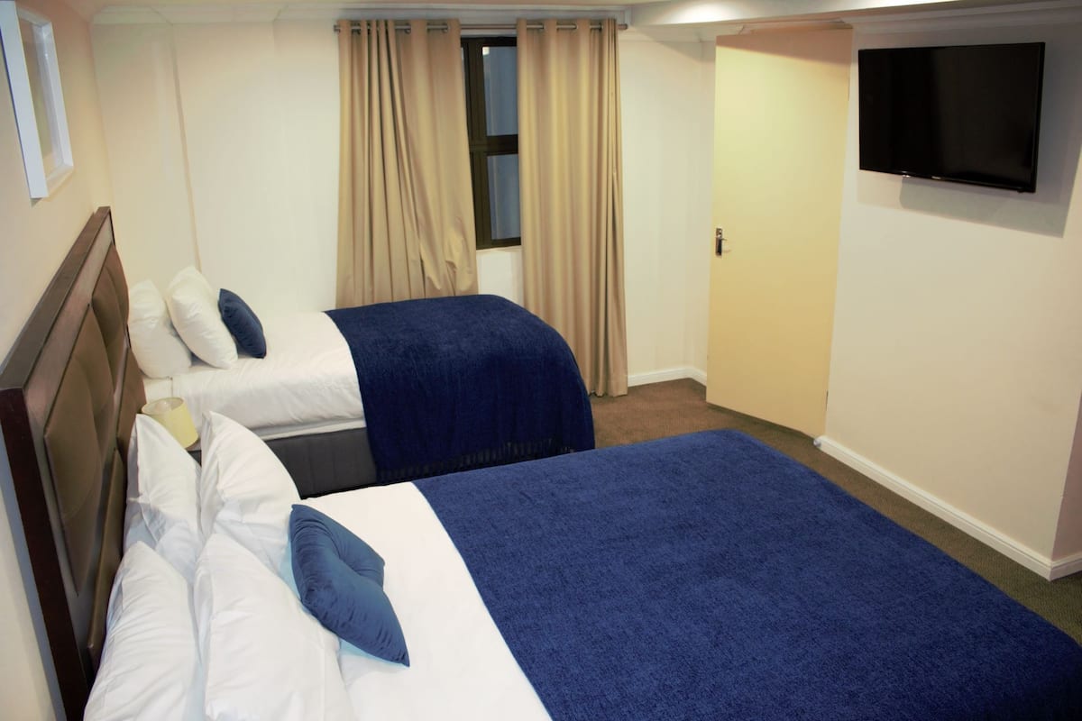 Ein Hotelzimmer mit zwei Betten, beigen Vorhängen, einem Flachbildfernseher und Teppichboden.